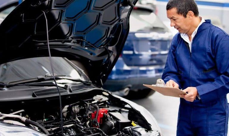 Man wearing a blue cover-all diagnosing a honda car with an open hood