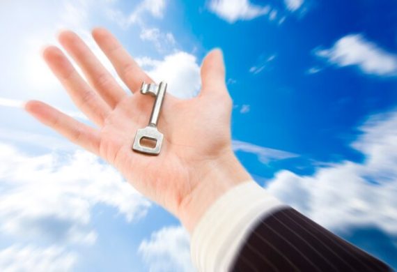 A hand in a business suit holds a vintage key—reminiscent of the Master Key System—against a bright blue sky with scattered clouds. The image evokes themes of opportunity and unlocking potential.