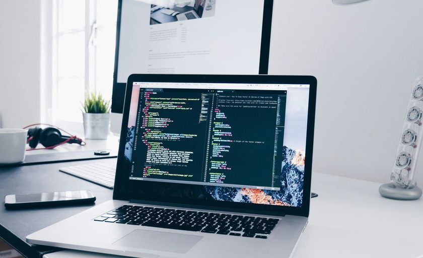 A MacBook with lines of code on its screen on a busy desk